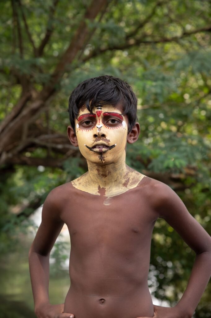 Portrait of a South Asian child with traditional face paint in a rural setting.